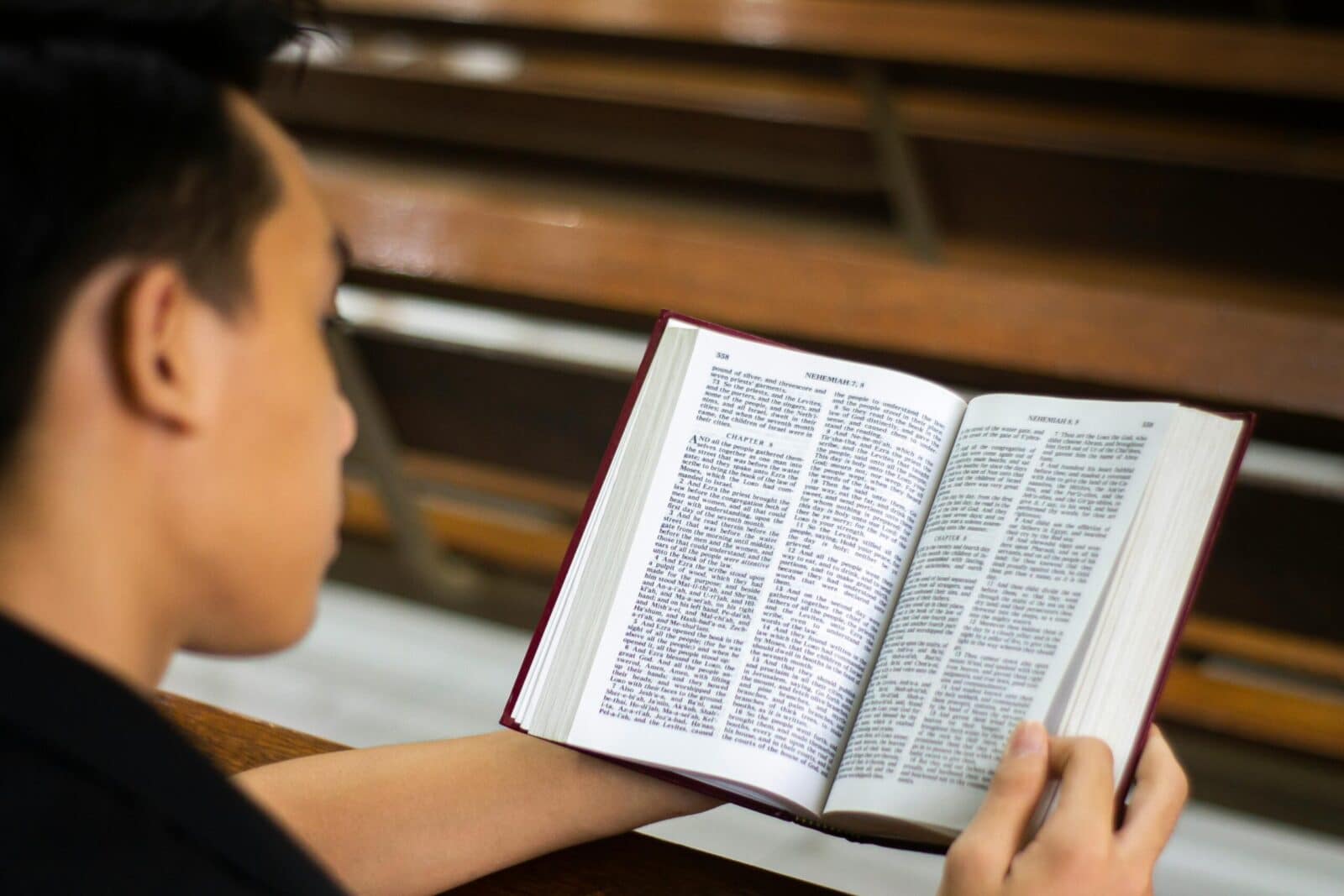 A man reading a book while sitting in a church interior, focusing on the open pages.