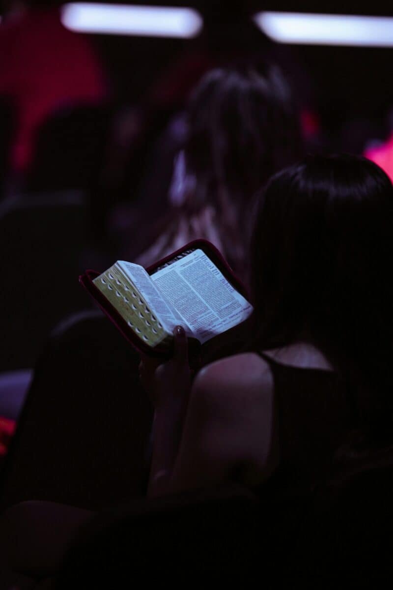 A young woman engrossed in reading a book while seated in a dimly lit room, captured in Jakarta.